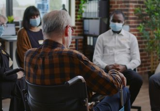 Senior man with disability attending aa group therapy session with people during pandemic